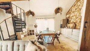 Una sala de estar acogedora con sofá, mesa de comedor y zona de cocina, con paredes de piedra y una escalera de caracol.