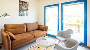 A living room with a brown sofa, a small round table, two white chairs, and a large window with blue frames. - Beautiful home in Rowy with house a panoramic view (Rowy)