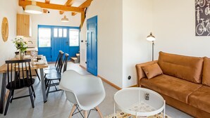 A dining area with a wooden table, chairs, and a vase of flowers. There is a blue door in the background and a brown sofa in the foreground. - Beautiful home in Rowy with house a panoramic view (Rowy)