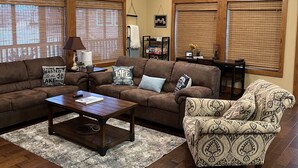 A living room with a brown sectional sofa, patterned armchair, wooden coffee table, and a ceiling fan.