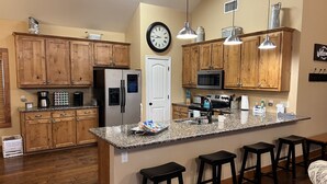 A kitchen with wooden cabinets, a stainless steel refrigerator, a microwave, and a large island with bar stools.