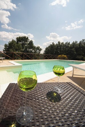 Un espace aménagé au bord de la piscine, avec deux verres d’une boisson verte, une table en métal et une vue sur une piscine entourée d’arbres.