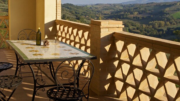 Eine Terrasse mit Tisch und Stühlen, einer Flasche und Blick ins Grüne.