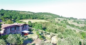 Una casa de piedra con balcón, rodeada de abundante vegetación y colinas.