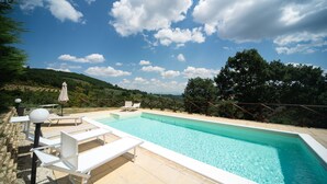 Ein Pool mit Liegestühlen und einer Pergola, umgeben von einer hügeligen Landschaft.