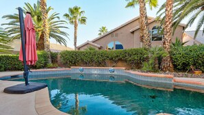 Una piscina de borde curvo, rodeada de palmeras y un edificio con techo de tejas.