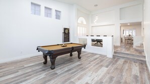 Una habitación amplia con mesa de billar, dardos y zona de comedor con una escalera.