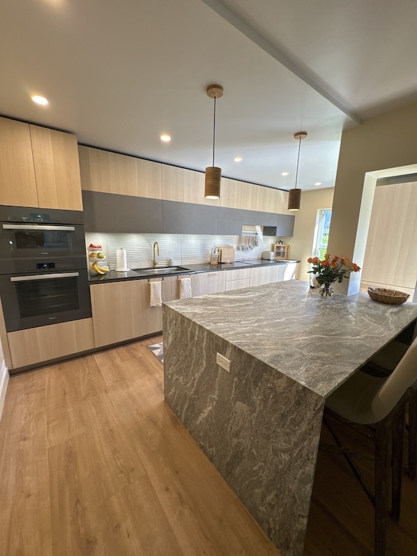 A modern kitchen with wooden cabinets, a marble island, and pendant lighting.