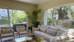 Un salon doté d’un sol carrelé à motifs hexagonaux, d’une table basse en verre, d’un canapé beige et d’une grande fenêtre donnant sur un paysage verdoyant.
