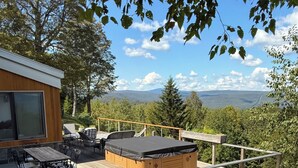 Une terrasse en bois avec un jacuzzi, un coin salon extérieur et une vue sur les montagnes.