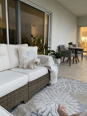 A white sofa with a small dog, a wicker chair, a table with a plant, and a patterned rug. - Gulf Stream Condo, private beach (Delray Beach)