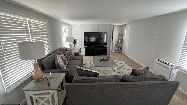 Ein Wohnzimmer mit grauem Sofa, einem Couchtisch und einem Fernseher. Eine Lampe steht auf einem Beistelltisch, und eine Heizung ist an der Wand angebracht.