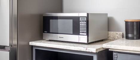 Una cocina con microondas sobre una encimera, un refrigerador de acero inoxidable y un cubo de basura negro.