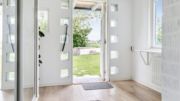 A room with a wooden floor, a door leading outside, and a window on the right.