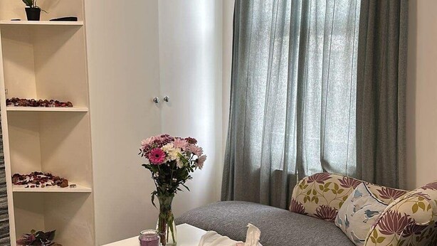 A neatly arranged bedroom with a bed, a bedside table with a tissue box and a vase of flowers, a chair, a sofa with floral cushions, and a wardrobe. - STUDIO FLAT IN ACTION  (London)