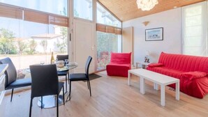Een moderne woonkamer met een rode bank, een witte salontafel en een eethoek met een tafel en stoelen.