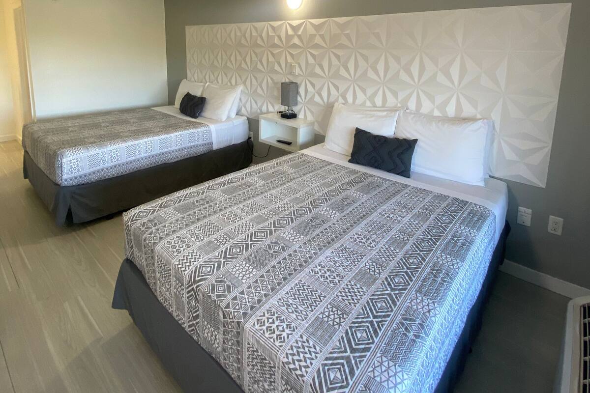 Ein Hotelzimmer mit zwei Betten, einem Kopfende mit geometrischem Muster, einem Nachttisch mit Lampe und einer Wandleuchte.