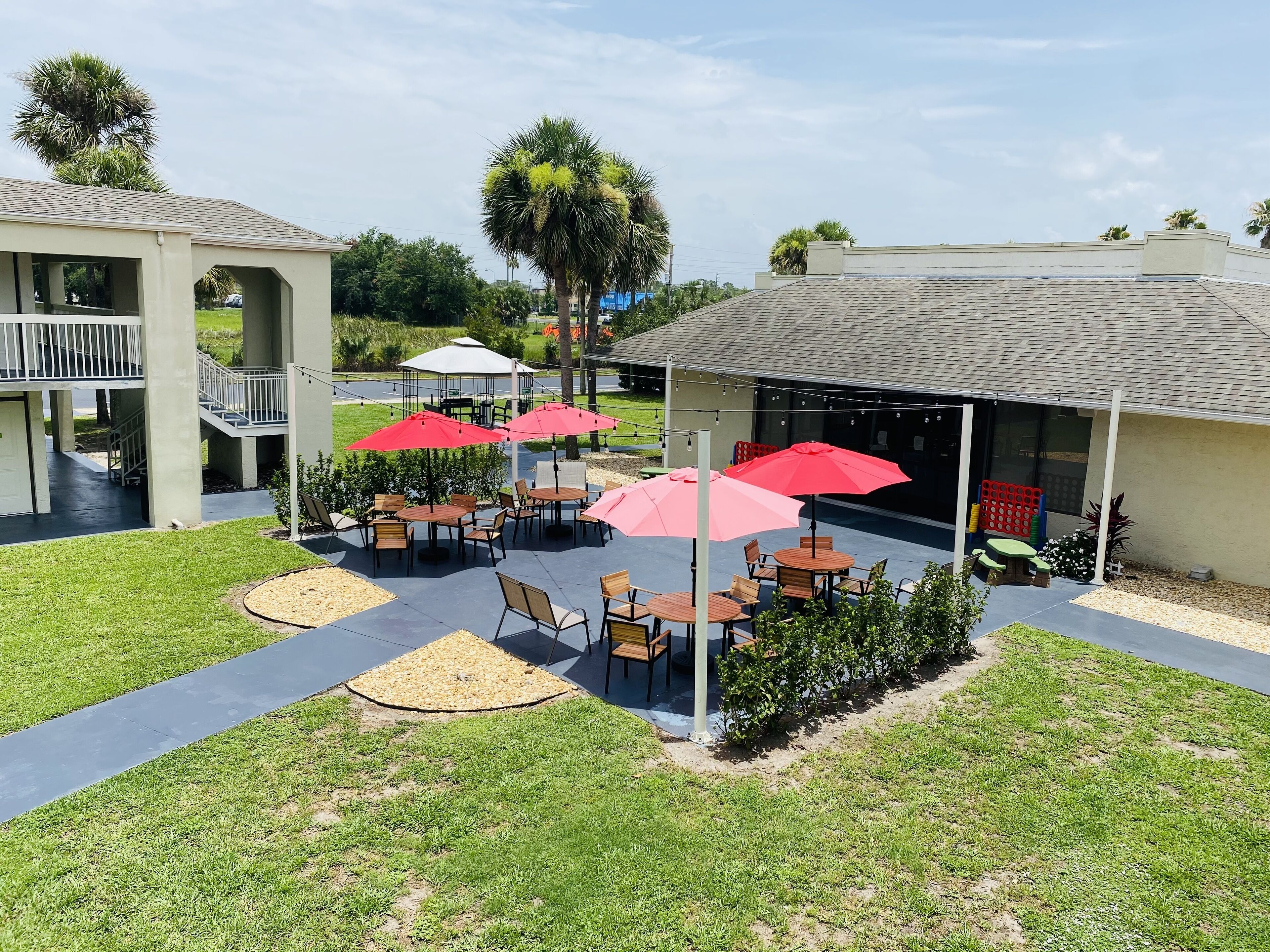 A courtyard with outdoor seating, palm trees, and a covered area with tables and chairs.
