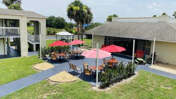 A courtyard with outdoor seating, palm trees, and a covered area with tables and chairs.