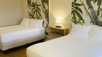 A hotel room with two single beds, a nightstand with a lamp, and a wall with a large plant mural.
