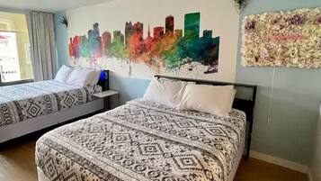 A hotel room with two beds, a cityscape mural, and a decorative wall hanging.