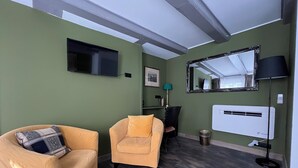 Un salon comprenant un canapé, un fauteuil, un téléviseur, un miroir, une lampe et un appareil de climatisation.