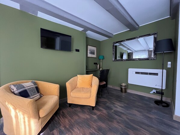 A living room with a sofa, armchair, TV, mirror, lamp, and air conditioning unit.