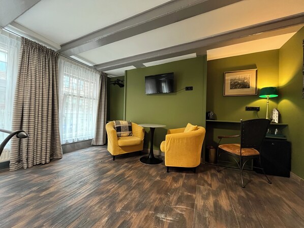 A room with two yellow armchairs, a small table, a desk, a chair, a lamp, and a television.
