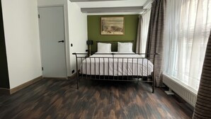 Une chambre à coucher avec un lit, une porte, un tableau au mur et une fenêtre avec des rideaux.