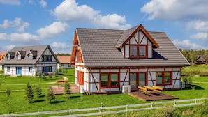 Een traditioneel vakwerkhuis met een schuine kap, een houten terras en een witte picket-omheining.