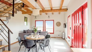 Een moderne leefruimte met een trap, een eethoek met een ronde tafel en stoelen, een bank, en deuren met rode randen.