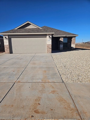 A residential garage with a brick exterior and a clear driveway leading to it. - New Build- 3 Bed, 2 Bath w Garage. (Lubbock)