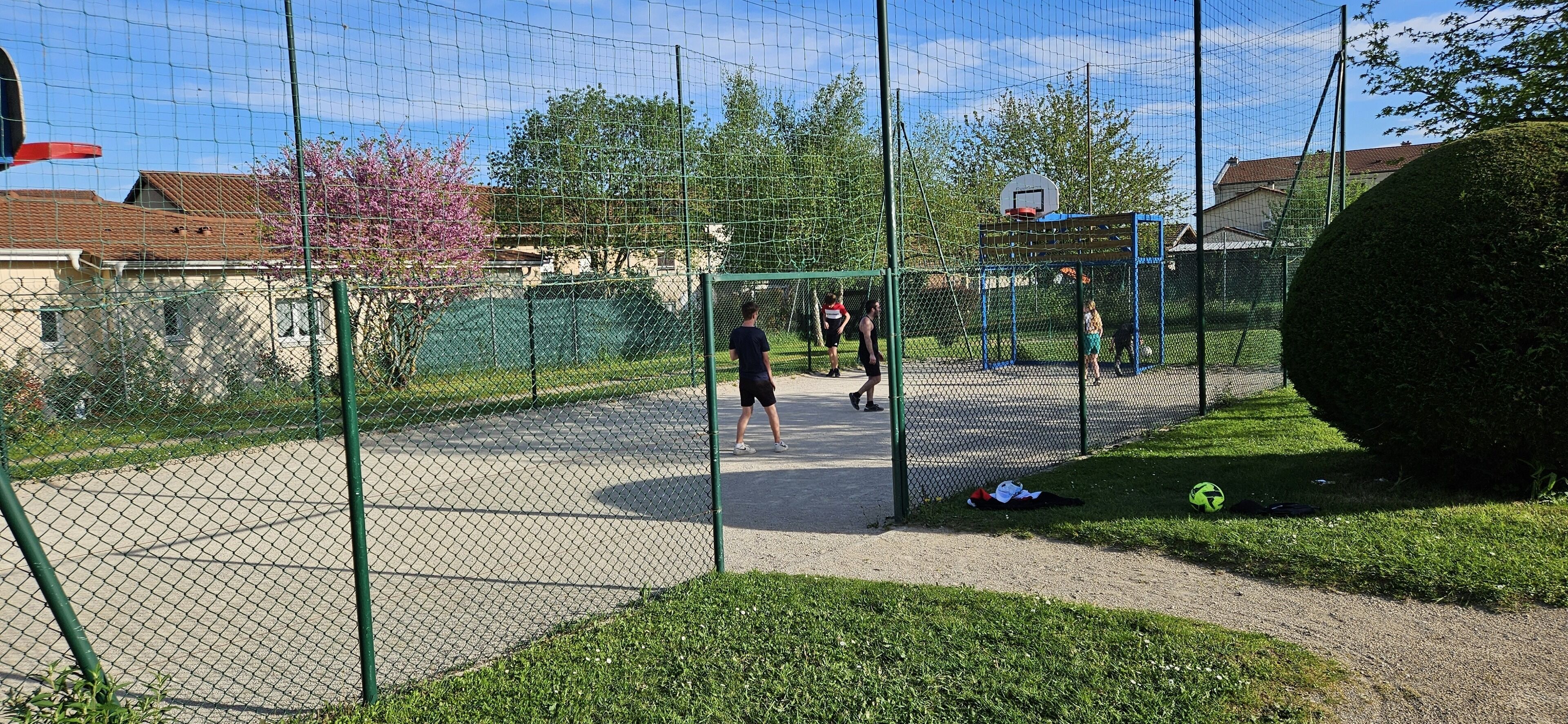 Ein eingezäunter Außenbereich mit Basketballfeld, Fußballtor und einem Spielbereich mit Netz.