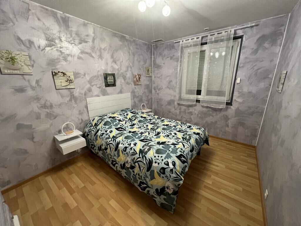 Un dormitorio con cama, mesita de noche, ventana con cortinas y una pared decorada con marcos.
