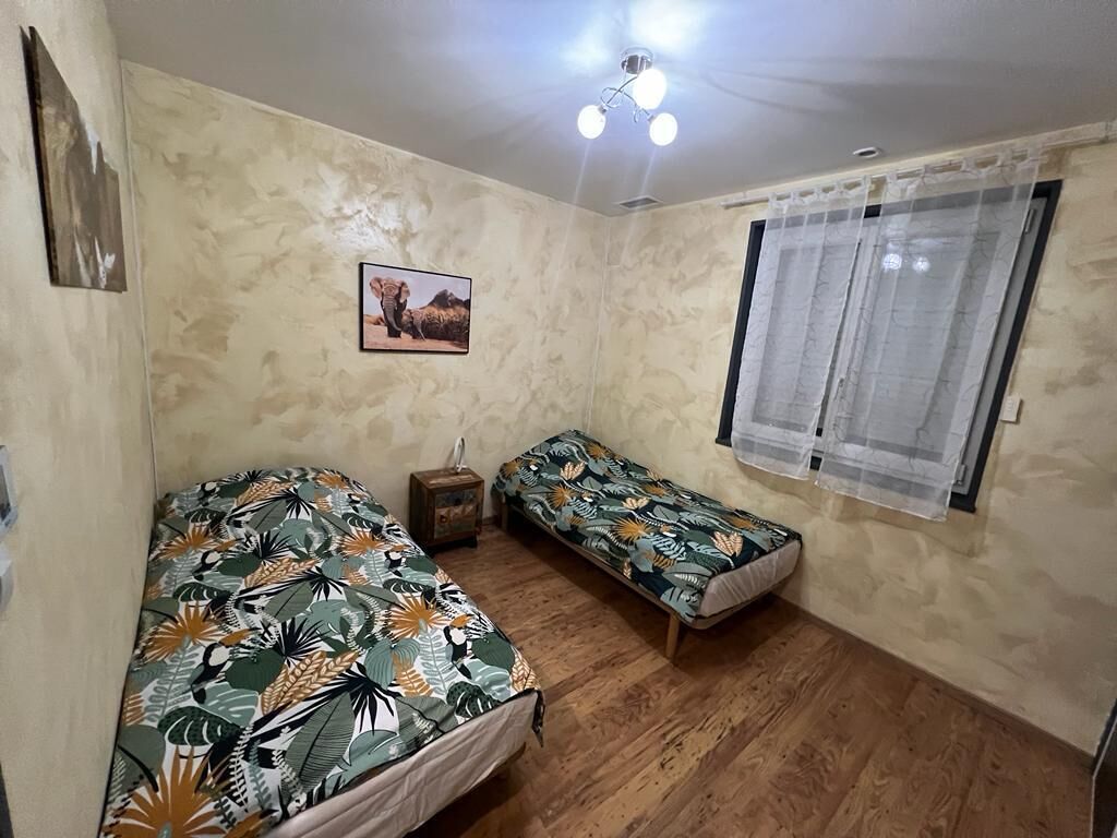 Una habitación pequeña con dos camas individuales, un ventilador de techo, una ventana con cortinas y un cuadro en la pared.
