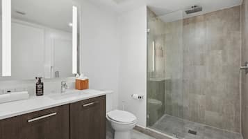 Un baño moderno con ducha envuelta en vidrio, inodoro blanco y tocador con espejo y lavamanos.