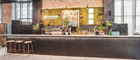 A modern coffee shop with a brick wall, a green wall with plants, a counter with a coffee machine, and bar stools.
