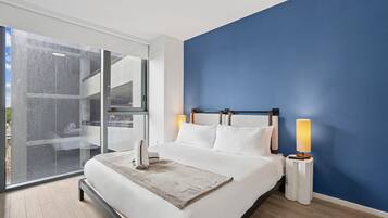 Una habitación de hotel moderna con una cama grande, un muro azul decorativo y vistas a través de un ventanal.