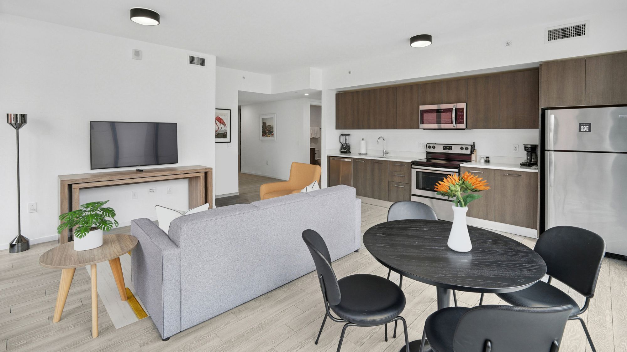 A modern apartment with a living room, dining area, kitchen, and a TV mounted on the wall.