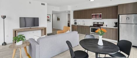A modern apartment with a living room, dining area, kitchen, and a TV mounted on the wall.
