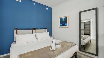 Ein Hotelzimmer mit einem großen Bett, einer blauen Akzentwand, einem gerahmten Bild und einem Spiegel, der den Raum reflektiert.