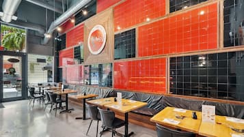 A restaurant interior with tables, chairs, a red-tiled wall, and a logo.