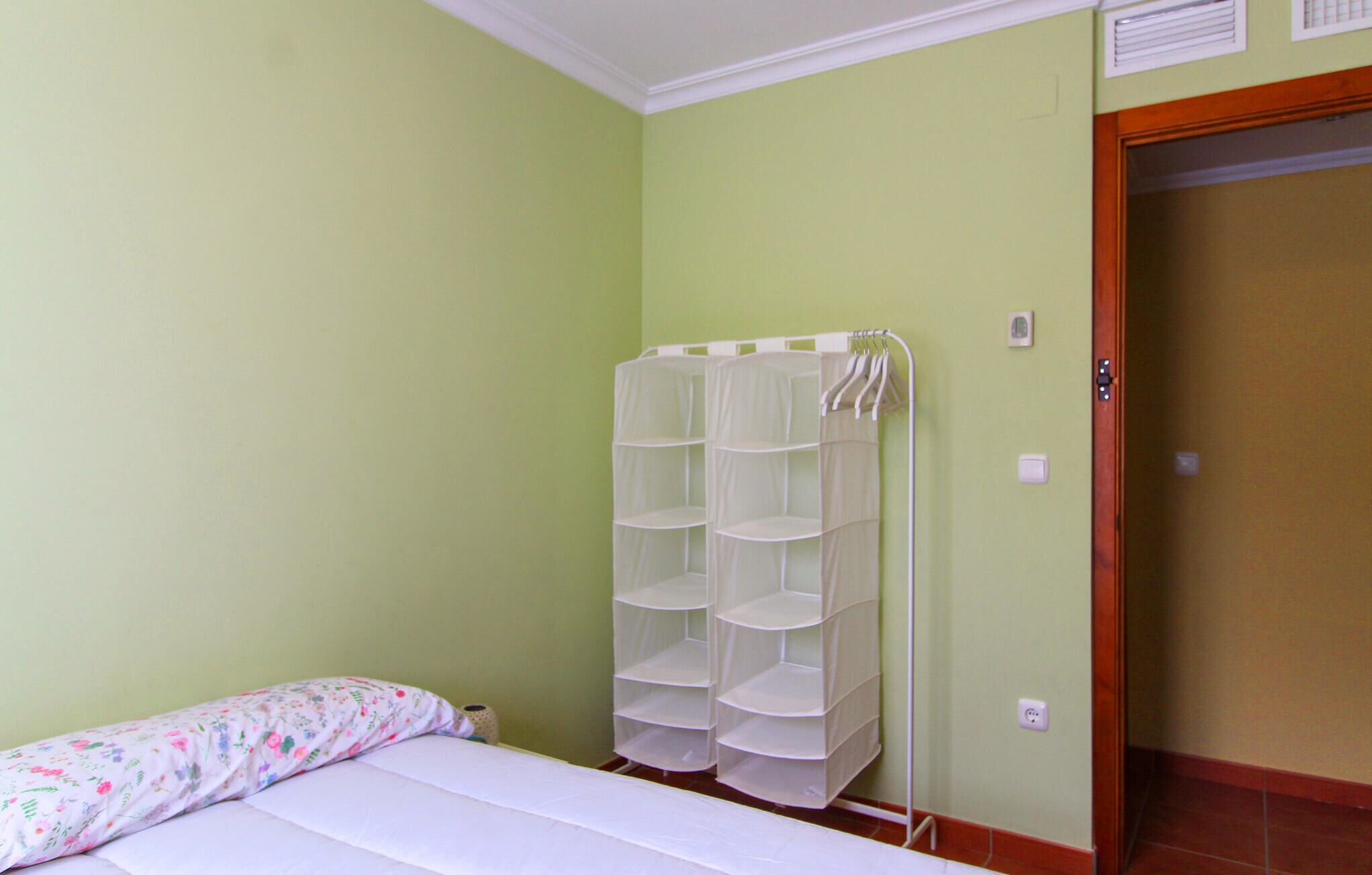 A bedroom with a bed, a white wall unit with shelves, and a door.