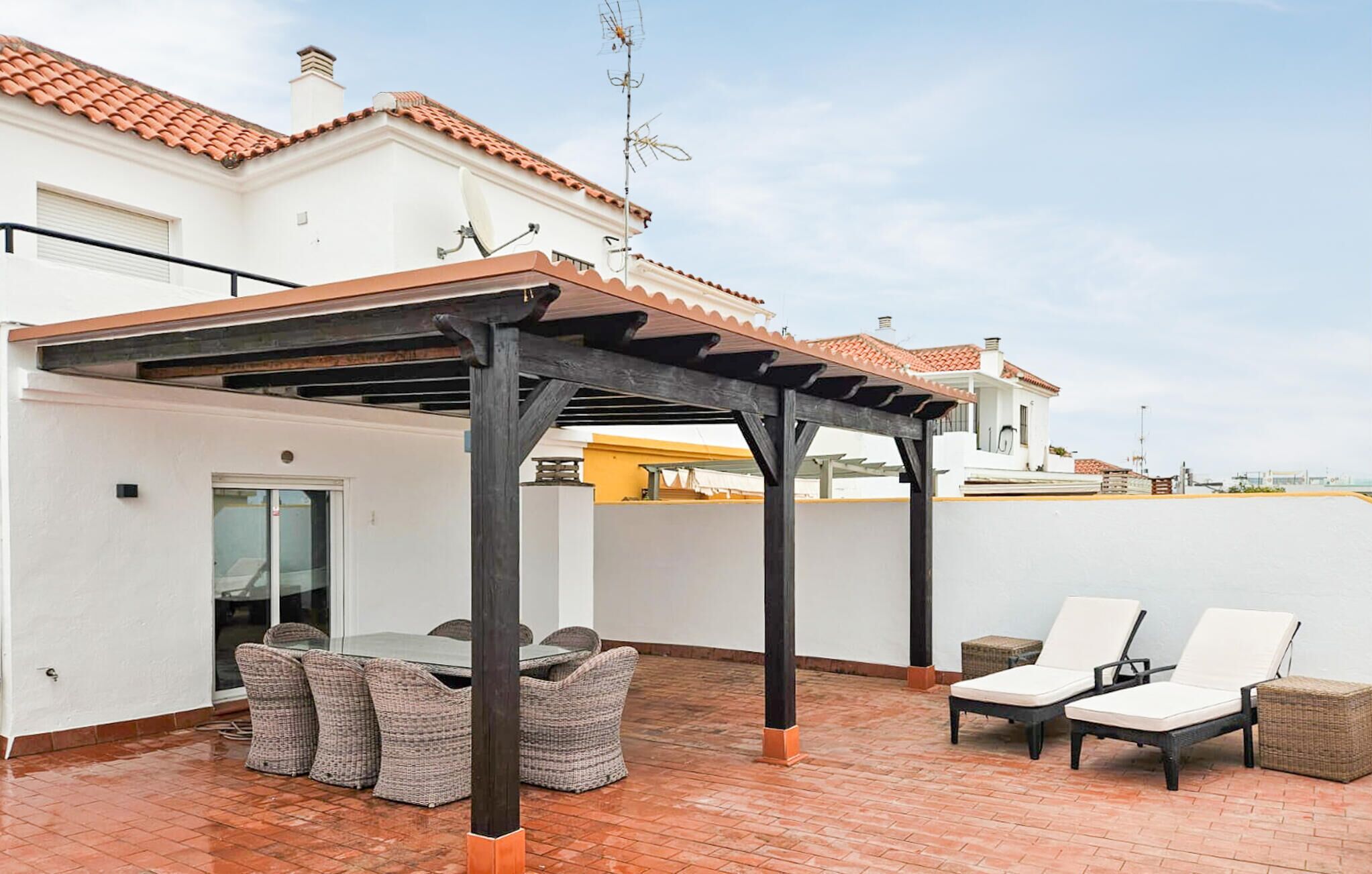 Una terraza en la azotea con pérgola, mobiliario de mimbre y sillones.