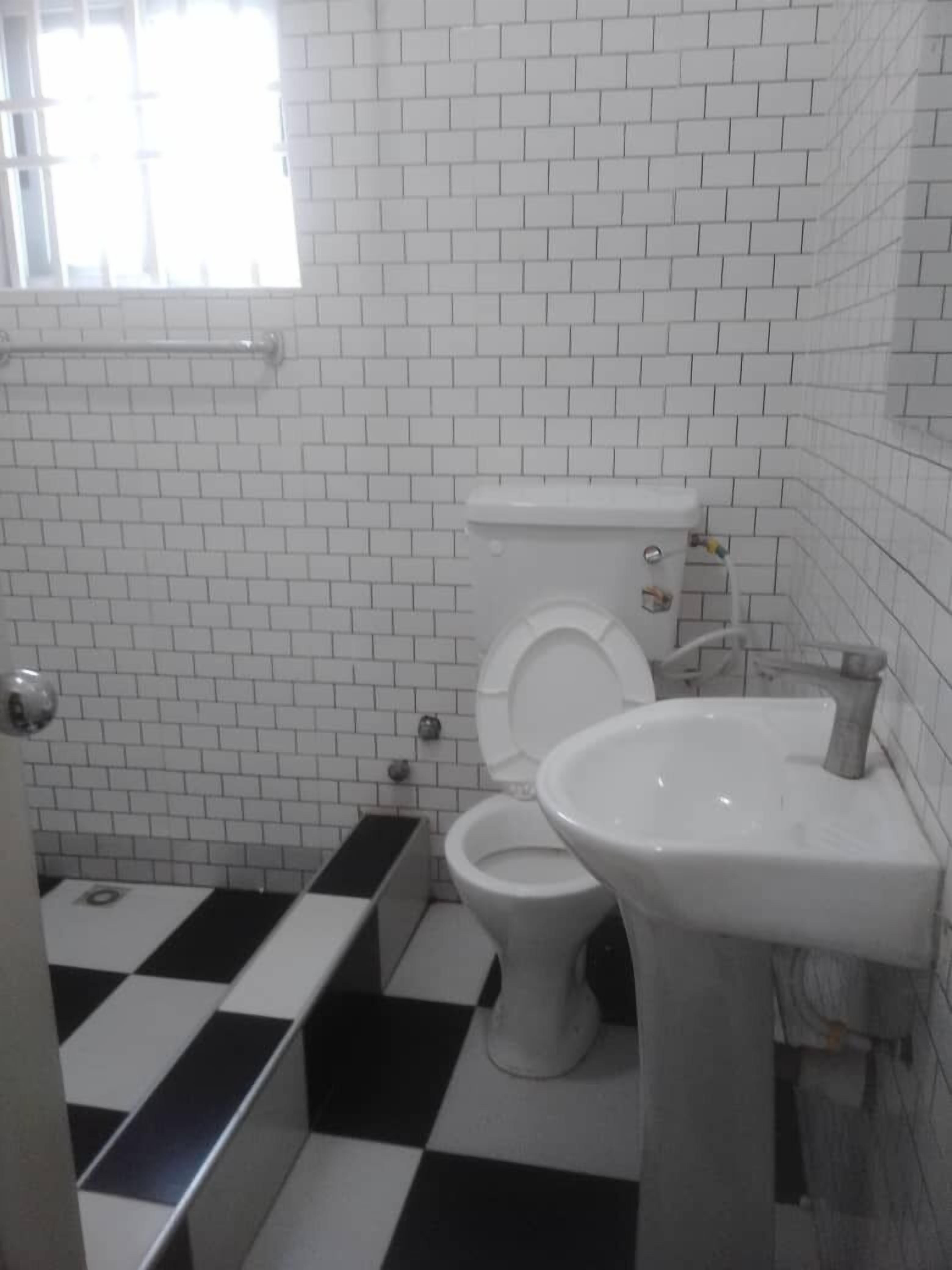 A bathroom with white tiled walls and floor, a toilet, a sink, and a checkered floor.