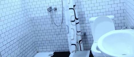 Un baño con piso a cuadros blanco y negro, un inodoro blanco y una zona de ducha con cortina blanca.