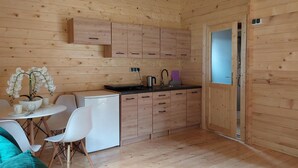 A compact kitchen with wooden cabinets, a small refrigerator, a sink, and a dining area with a table and chairs. - 1 bedroom beach front home in Pobierowo (Pobierowo)