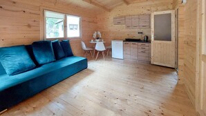 A cozy cabin interior with a blue sofa, a small dining table with chairs, a kitchenette, and a large window. - 1 bedroom beach front home in Pobierowo (Pobierowo)