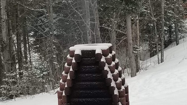 A snow-covered outdoor fireplace with a brick structure and a fire burning inside, surrounded by a snowy forest. - Bathurst New Brunswick Access to snowmobiles trail and ATV. (Saint-Laurent)
