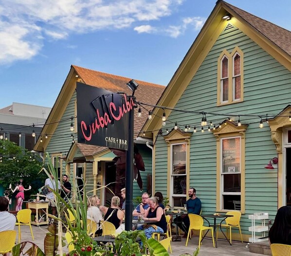 An outdoor seating area with tables and chairs, a sign for 'Cuba Cuba Cafe & Bar', and a building with a green facade and a yellow roof. - Chic Apt w/parking - Walk to Capitol, Convention Center, museums & shops! (Denver)